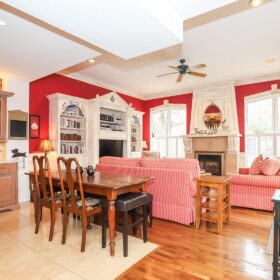 An image of the large family room in the back of the Meritage House. Couches frame a floor to ceiling fireplace, overlooked by the full size kitchen and dining area.